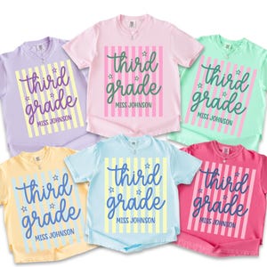 May include: A collection of six short-sleeved t-shirts in various pastel colors: lavender, pink, mint green, yellow, light blue, and hot pink. Each shirt features the text "third grade" in a script font, with "Miss Johnson" below, and vertical stripes.