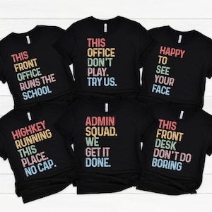 May include: Six black t-shirts with colorful text. The shirts have phrases like "This Front Office Runs The School," "This Office Don't Play. Try Us," and "Happy to See Your Face." The shirts are likely for a school or office.