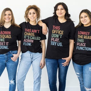 May include: Four people wearing black t-shirts with colorful text. The shirts have phrases like "ADMIN SQUAD. WE GET IT DONE" and "THIS OFFICE DON'T PLAY. TRY US." They are wearing blue jeans. The background is white.