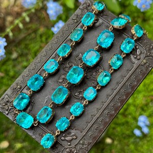 May include: A bracelet featuring multiple rectangular, faceted, bright turquoise-blue glass stones set in gold-toned metal frames. The stones are linked together in a continuous chain, showcasing a vibrant, translucent color and reflective surfaces.