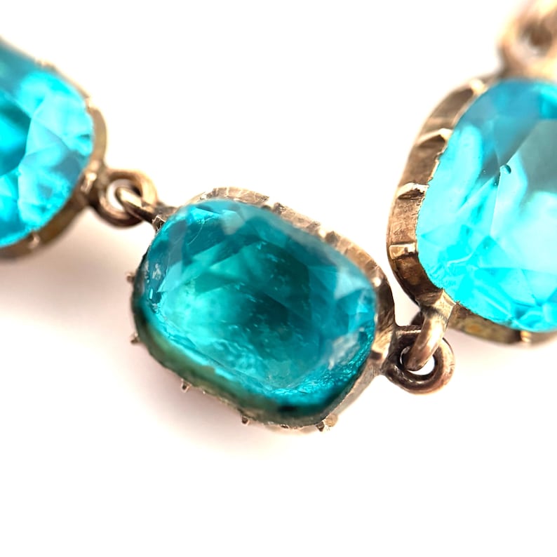 May include: A bracelet featuring multiple faceted, rectangular, bright turquoise blue stones set in metallic frames. Each stone is connected by small metal jump rings, creating a flexible chain of vibrant, translucent blue gems with visible facets.