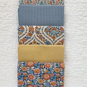 May include: Five folded fabric pieces with floral and striped patterns. The fabrics feature a variety of colors, including blue, orange, pink, and yellow. The fabrics are stacked on a white, quilted surface.
