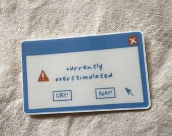 May include: A blue and white sticker with a computer error message that says "currently overstimulated". The sticker has two buttons that say "cry!" and "nap!" and a red exclamation point.