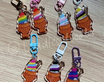 Puede incluir: Seis llaveros de acrílico coloridos con un personaje de dibujos animados en un taiyaki con helado. Cada llavero tiene un esquema de color diferente y una bandera diferente en el helado. Los llaveros están unidos a llaveros de metal.