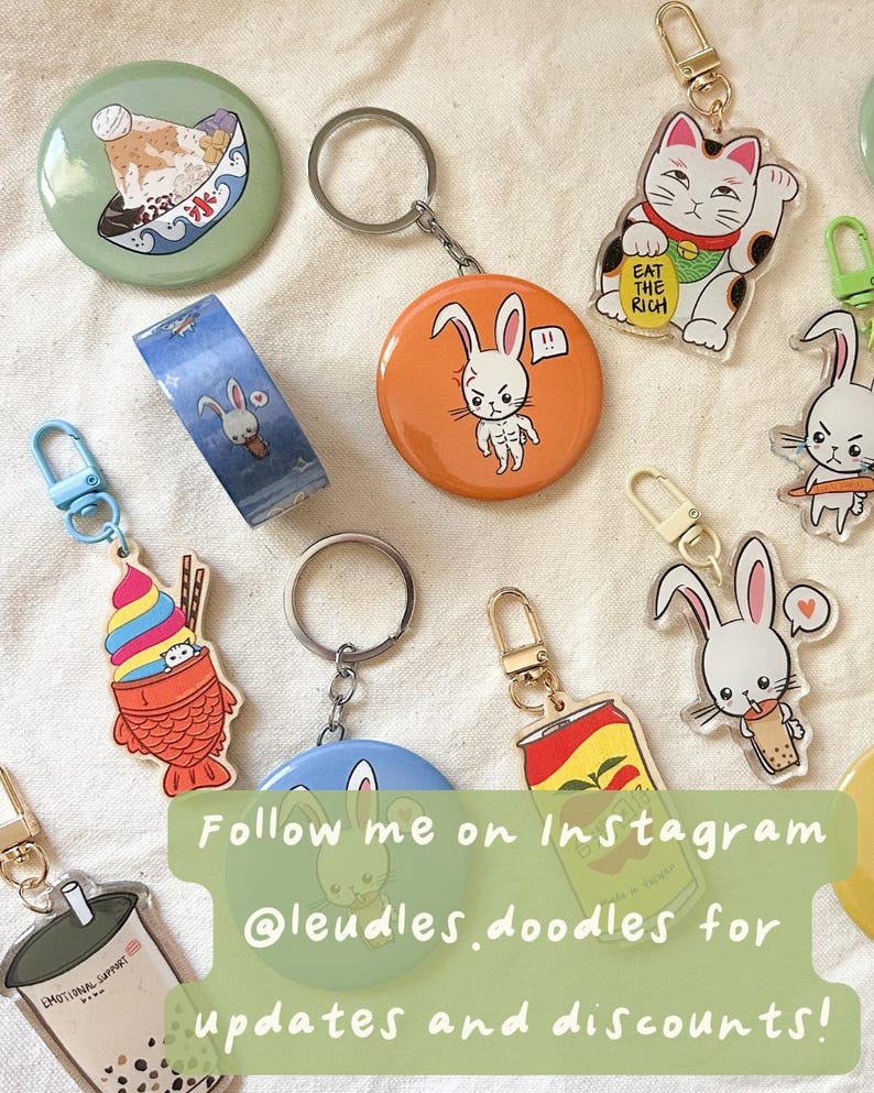 May include: Collection of colorful keychains and buttons with various designs, including a lucky cat, bunny characters, and a bubble tea cup. The image also includes a roll of washi tape with a bunny design. Text on the image reads "EAT THE RICH" and "EMOTIONAL SUPPORT".