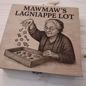 May include: A wooden box with a brown background and a black and white illustration of a woman holding a tray of small objects. The text "Mawmaw's Lagniappe Lot" is printed in black on the box.