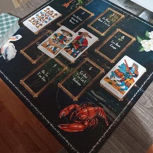 May include: A tarot card spread on a dark blue mat with gold-framed card positions. The spread includes various tarot cards with illustrations and French text. A red lobster illustration is in the lower right corner.