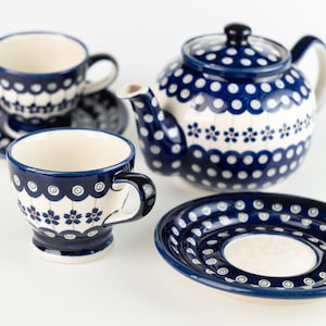 Könnte beinhalten: Ein Keramik-Teeservice mit blau-weißem Blumenmuster. Das Set besteht aus einer Teekanne, zwei Tassen und zwei Untertassen. Die Teekanne hat einen Deckel und einen Henkel. Die Tassen und Untertassen haben einen gewellten Rand. Auf weißem Hintergrund.