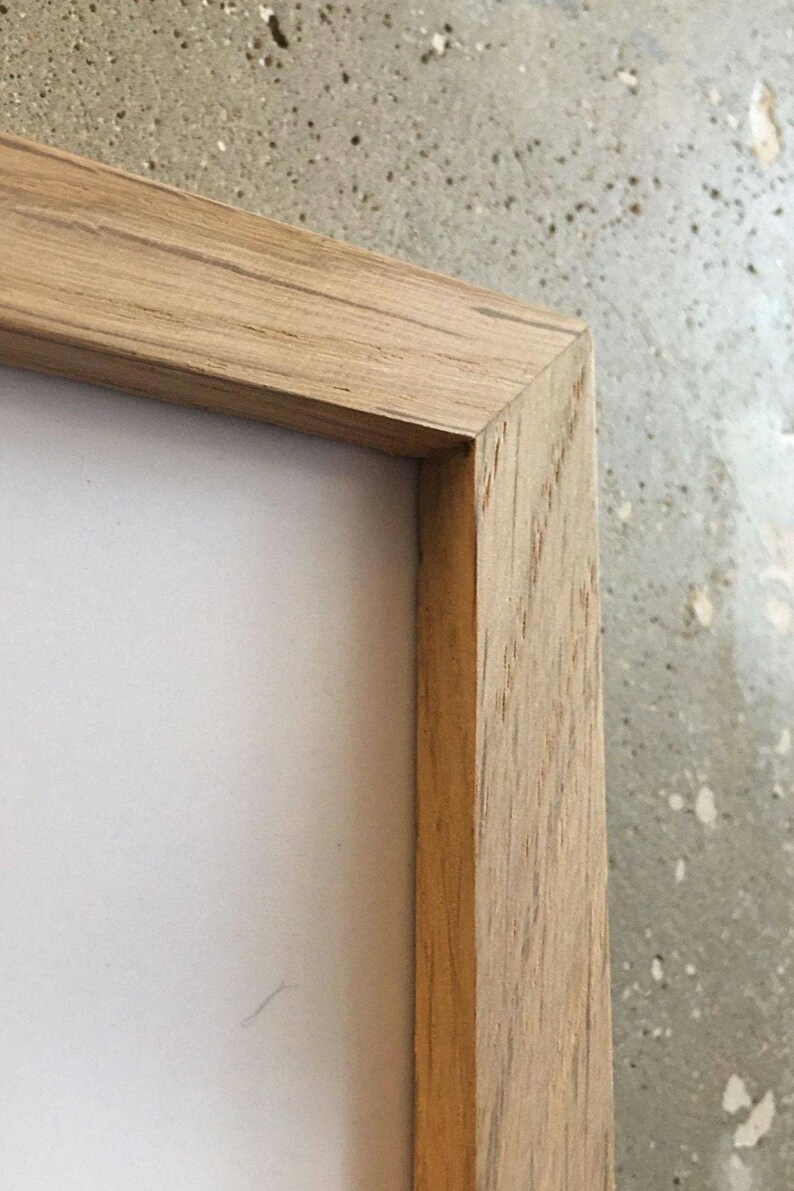 May include: Close-up of the corner of a natural wood picture frame. The frame is made of light brown wood with a visible grain pattern.