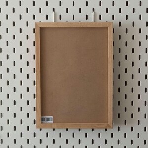 May include: A brown wooden picture frame with a white background. The frame is hanging on a white pegboard wall.