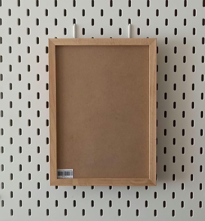 May include: A brown wooden picture frame with a white background. The frame is hanging on a white pegboard wall.
