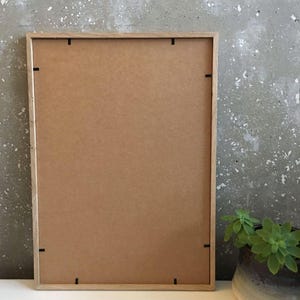 May include: A wooden picture frame with a brown cardboard backing. The frame has a simple design and is ready to display a photo or artwork.