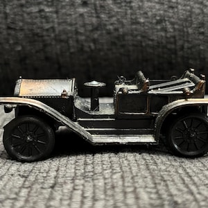 May include: A miniature antique car model in black and bronze. The toy car features spoked wheels, a steering wheel, and a detailed interior. The car is a vintage style, likely from the early 20th century.