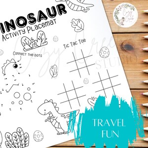 May include: A black and white dinosaur activity placemat with the text "DINOSAUR ACTIVITY PLACEMAT". The placemat includes connect-the-dots, tic-tac-toe, and other activities. The words "TRAVEL FUN" are also visible.
