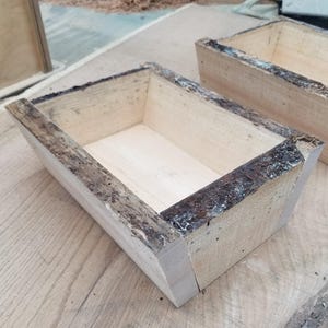 May include: Two wooden boxes with a rustic, natural finish. The boxes are made of unfinished wood with a dark brown stain around the edges. The boxes are empty and ready to be filled.