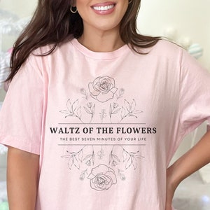 May include: A light pink t-shirt with a black floral design and the text "Waltz of the Flowers" and "The Best Seven Minutes of Your Life".