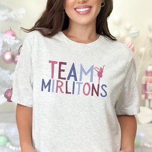 May include: A gray t-shirt with the text "TEAM MIRLITONS" in pink, blue, and purple letters. A pink silhouette of a ballerina is in the middle of the text.