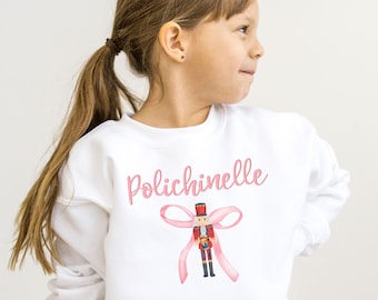 May include: White sweatshirt with a pink bow and a nutcracker illustration. The text "Polichinelle" is printed on the sweatshirt.