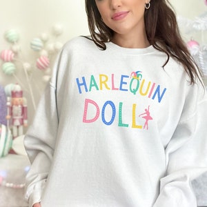 May include: White sweatshirt with the text "HARLEQUIN DOLL" in colorful letters with a jester hat and a ballerina graphic.