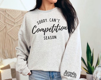 May include: A gray sweatshirt with the text "Sorry. Can't. Competition Season" on the front and "Gymnastics Coach" on the sleeve.