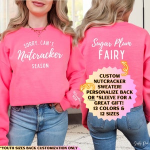 May include: A bright neon pink crewneck sweatshirt featuring white text on the front that reads SORRY. CAN'T. Nutcracker SEASON. The back of the sweatshirt displays the white text Sugar Plum FAIRY. The sleeve includes the text Nutcracker MOM.