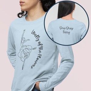 May include: Light blue long-sleeved t-shirt with a black line drawing of a ballerina dancing in a flower on the front. The text "Waltz of the Flowers" is written vertically on the right side of the image. The back of the shirt has the text "Dew Drop Fairy" in black.