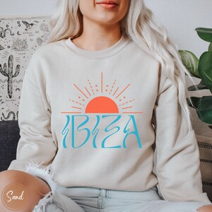 May include: A beige sweatshirt with a blue and orange graphic of a sun and the word "IBIZA" on the front.