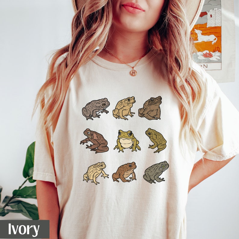May include: Ivory t-shirt with a graphic of nine different frogs in various poses. The frogs are brown, green, and tan.