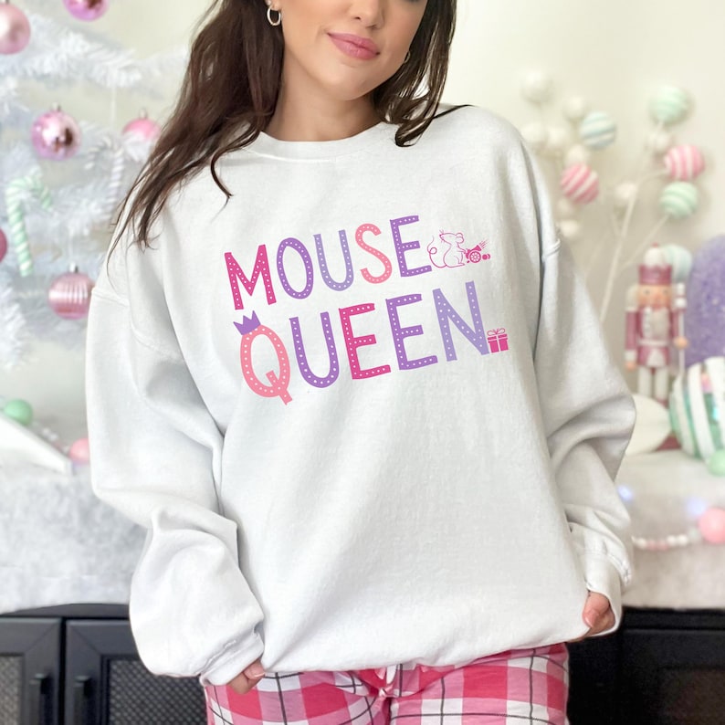 Op de afbeelding: Witte sweatshirt met de tekst "MOUSE QUEEN" in roze en paars, met een kroongrafiek op de letter "Q" en een muisgrafiek. Een casual, comfortabele stijl.