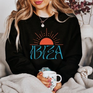 May include: Black sweatshirt featuring a graphic of a red sun with blue rays and the word "IBIZA" in blue lettering.