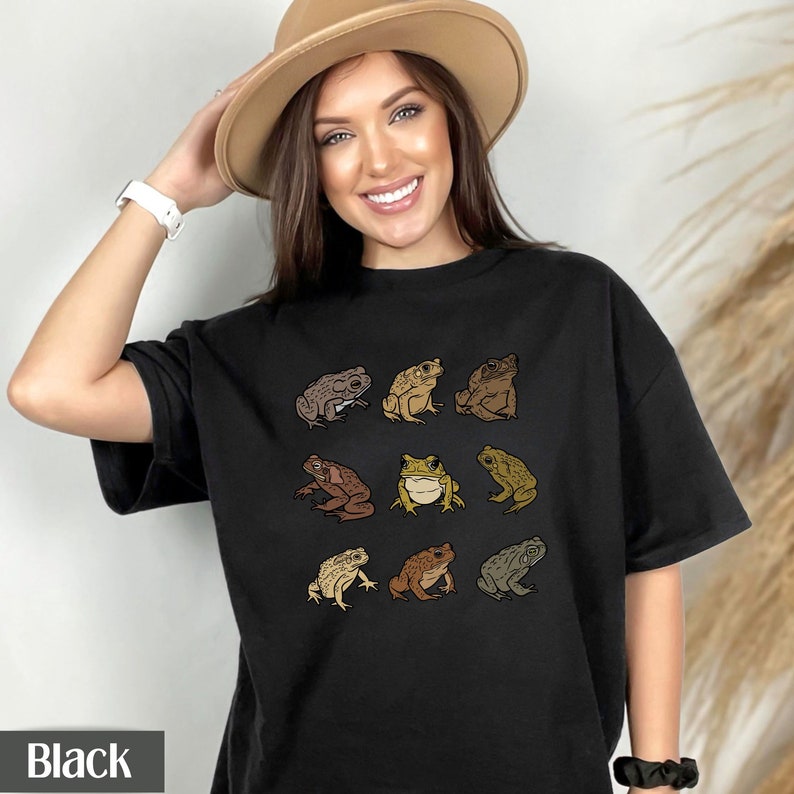 May include: Black t-shirt with a graphic of nine brown toads in different poses. The toads are outlined in black and have a vintage look.