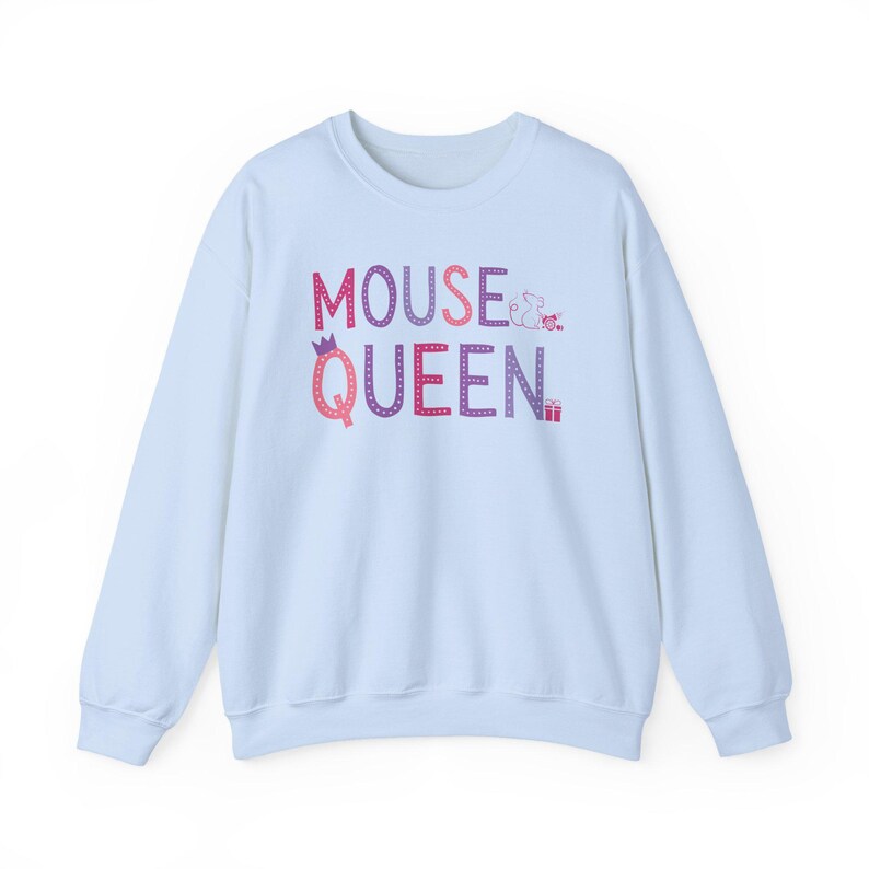Op de afbeelding: Een lichtblauwe sweatshirt met de tekst "MOUSE QUEEN" in een kleurrijk, gestippeld lettertype. Het woord "QUEEN" heeft een kroon boven de letter "Q". Een kleine muis en een cadeaudoosje zijn ook aanwezig.
