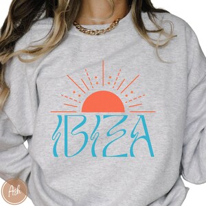 May include: A grey sweatshirt with a blue and orange graphic design of a sun and the word "IBIZA".
