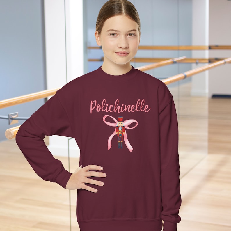 May include: Burgundy sweatshirt with a pink bow and a nutcracker illustration. The text "Polichinelle" is printed on the sweatshirt.