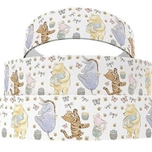 May include: Three stacked white ribbons with a repeating pattern of Winnie the Pooh characters, butterflies, and honey pots. The characters include Pooh Bear, Tigger, Eeyore, and Piglet. The ribbons are likely for crafting or gift wrapping.