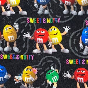 May include: A black fabric featuring a repeating pattern of colorful M&M's characters. The characters are in various poses and colors, including red, yellow, blue, and green. The words "SWEET & NUTTY" are also displayed in a rainbow font.