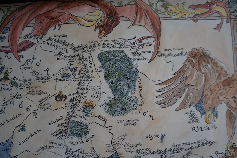 May include: A hand-drawn fantasy map on parchment paper featuring a large red dragon flying across the top and a brown eagle on the right side. The map displays various geographical locations, mountain ranges, and forests with black ink text labels.