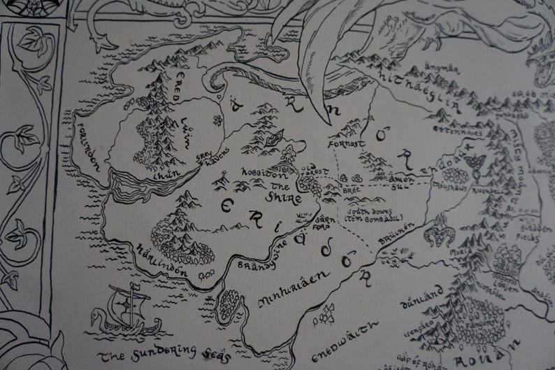 May include: A black and white ink illustration of a fantasy map featuring geographical regions labeled Ered Luin, The Shire, and Minhiriath. The map includes detailed drawings of mountain ranges, forests, and a sailing ship in The Sundering Seas.