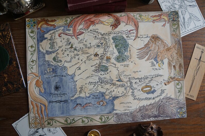 May include: A hand-drawn map of Middle-earth on parchment-style paper, featuring intricate ink and watercolor illustrations of a dragon, a large eagle, a horse, and the One Ring. The map includes detailed geographical labels and a compass rose.