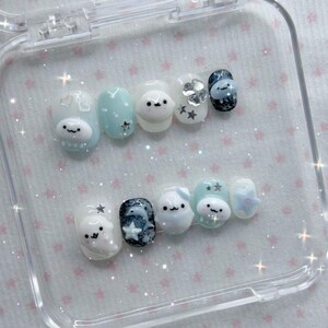 Peut inclure: Un ensemble de dix faux ongles dans un &eacute;tui en plastique transparent. Les ongles pr&eacute;sentent divers motifs, notamment des personnages de dessins anim&eacute;s, des &eacute;toiles et des pois, dans des tons de bleu, de blanc et de noir. Les ongles sont ovales et ont une finition brillante.