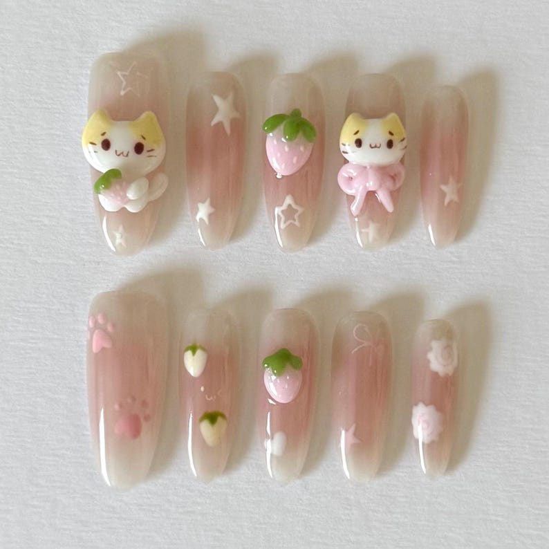 May include: Set of ten pink and white false nails with various designs. The designs include a cat holding a strawberry, a strawberry, a paw print, and a flower.