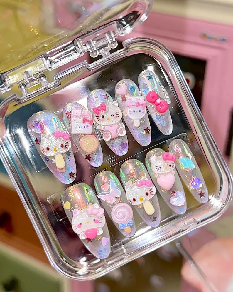 Peut inclure: Un ensemble de dix faux ongles dans un &eacute;tui en plastique transparent. Chaque ongle pr&eacute;sente une base holographique avec divers embellissements 3D, notamment des figurines Hello Kitty, des n&oelig;uds, des c&oelig;urs et des &eacute;toiles. Les ongles sont de formes vari&eacute;es.