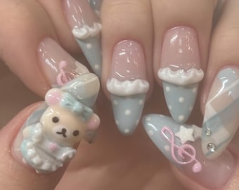 May include: Close-up of light blue and white nail art with a 3D bear charm, polka dots, and a musical note design.