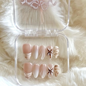 May include: A set of press-on nails in a clear plastic case. The nails feature a variety of designs, including solid nude, ombre, seashell, and striped patterns. The case has the text "14th STREET" printed on the top.