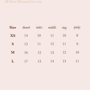 May include: A nail size guide from 79th Street, with measurements in millimeters. The guide lists sizes XS, S, M, and L, with corresponding thumb, index, middle, ring, and pinky measurements. The text is in a serif font on a light beige background.