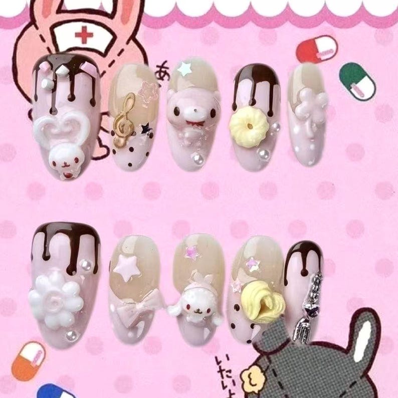 May include: A set of ten artificial nails with various designs. The nails feature a light pink base with embellishments such as cartoon characters, musical notes, bows, and flowers. Some nails have a chocolate drizzle effect.