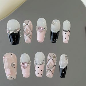 May include: Ten pink and white false nails with different designs. Some nails have black polka dots, others have a black and white plaid pattern, and some have a black and white lace design. Some nails have rhinestones and a pink heart.