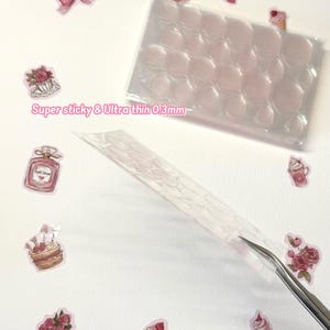 May include: A sheet of clear, ultra-thin adhesive dots, 0.3mm thick, with a honeycomb pattern. The sheet is packaged in a clear plastic bag. The adhesive dots are designed for crafts and scrapbooking.