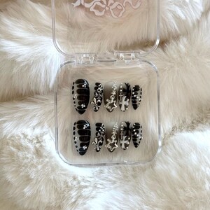 May include: A clear plastic case with black and white press-on nails. The nails have a floral design with silver accents.