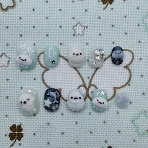 Peut inclure: Un ensemble de dix faux ongles avec divers motifs. Les ongles pr&eacute;sentent une palette de couleurs bleu clair, blanc et marine. Certains ongles comportent des personnages de dessins anim&eacute;s en 3D, des &eacute;toiles et un dauphin. D'autres ont des ornements argent&eacute;s. Les ongles sont dispos&eacute;s sur une surface &agrave; motifs bleu clair.